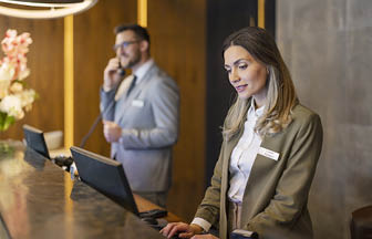 Attractive female receptionist working at hotel counter with her colleague in the background. Hotel concierge.